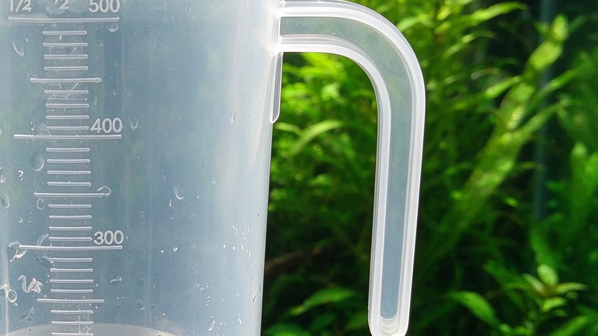 Close-up of an aquarium measuring cup with handle showing molded graduated scale marks