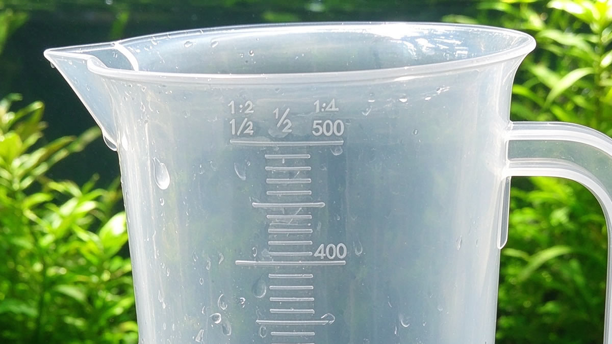Close-up of molded ml measurement marks and ratio scale on a clear aquarium measuring cup with spout